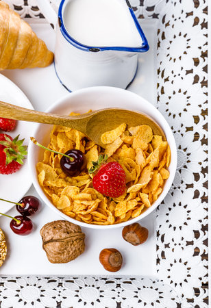Breakfast with cornflakes berry and muesli croissant on white tray.