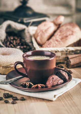 Cup fragrant hot coffee with bean chocolate sweet and croissant in vintage rustic style cinnamon steam smoke on wooden board for bracing morning breakfast.の写真素材