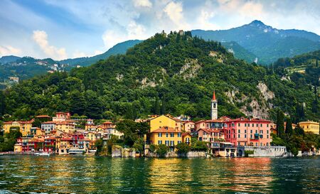 Varenna, Italy. Picturesque town at lake Como. Colourful motley Mediterranean houses at stone beach coastline among green trees. Popular health resort and touristic location. Summer day landscape.の写真素材
