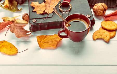 Cup coffee with book in leather binding autumn dry leaf and warm scarf on white wooden boardの写真素材
