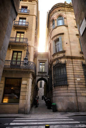 Barcelona, Catalonia, Spain. Romantic narrow residential bystreet in Gothic Quarter. Antique street lamp at wall of old house, parked motorbikes and arch with window between buildings.の写真素材