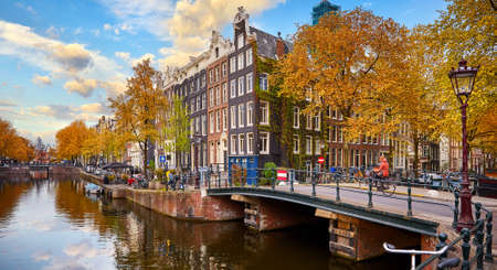 Netherlands Amsterdam. View at river Amstel with traditional houses at bank and boats at water canal. Scenic cityscape. Spring day with blue sky and white clouds.の写真素材
