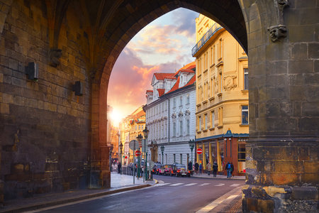 Prague, Czech Republic. Sunset in old town through medieval arch in Powder Gate tower of vintage european street. Scenic urban landscape with sun.の写真素材