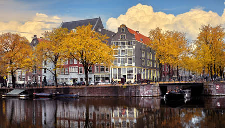 Netherlands Amsterdam. View at river Amstel with traditional houses at bank and boats at water canal. Scenic cityscape. Spring day with blue sky and white clouds.の写真素材