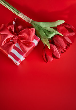 Festive card at Valentines day. Bouquet tulips and gift with bow at red background top view.の写真素材