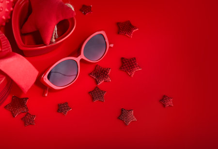Festive card. Sunglasses at red background with star and soft toy. Top view.の写真素材