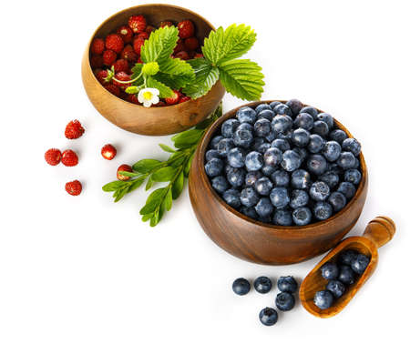 Berry blueberry and wild strawberry in wooden dish with green leaves and flower. Fruity still life. Healthy eating, isolated on white background.の写真素材