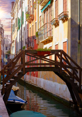 Venezia, Veneto, Italy. Vintage wooden bridge with stairs over canal between houses of traditional italian architecture. Romantic place and evening sunset.の写真素材
