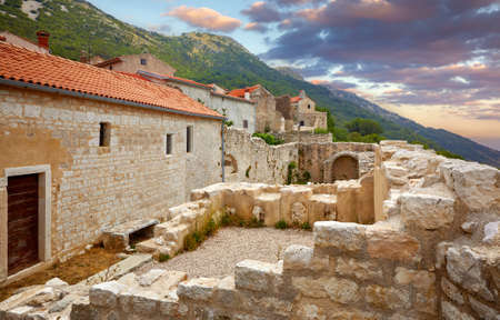 Croatia Istria. Ancient abandoned medieval town Plomin. Old stone street with ruined walls houses and stairs overgrown by ivy plants.の写真素材
