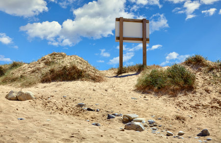 Sandy sand-dune with grass at coast beach of Atlantic ocean in Portugal with blue sky and clouds.