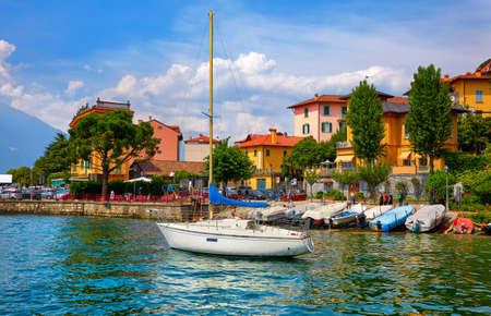 Varenna, Italy. Picturesque town at lake Como. Colourful motley Mediterranean houses at stone beach coastline among green trees. Popular health resort and touristic location. Summer day landscape.の写真素材