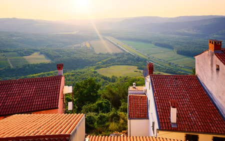 Motovun Croatia. View with high hill at green lowland. Red tegular roof with chimney. Picturesque landscape. Sunset over forest and background.の写真素材