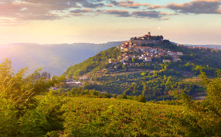 Antique city Motovun Croatia Istria. Picturesque panorama age-old village at hill with pink cloud and sunny light and authentic home with red tegular roof and green vineyard garden.の写真素材
