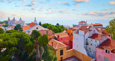 Lisbon Portugal. Panoramic top view at red tiled roofs of houses in antique historical district Alfama with cathedral on top of knoll. Sunny day with blue sky and clouds.の写真素材