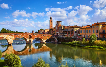 Panoramic view to Bridge Ponte Pietra in Verona on Adige river Veneto region Italy. Sunny summer day panorama and blue dramatic sky with clouds. Ancient european italian terracotta color housesの写真素材