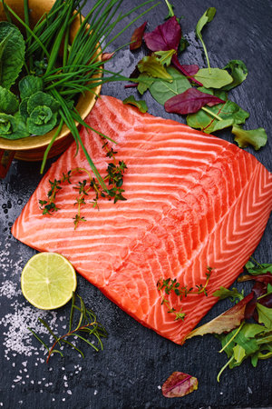 Fresh steak salmon red fish on black stone blackboard with knife cuted lime and salt olive oil fresh spicy herbs. Top view at gray concrete surface.の写真素材
