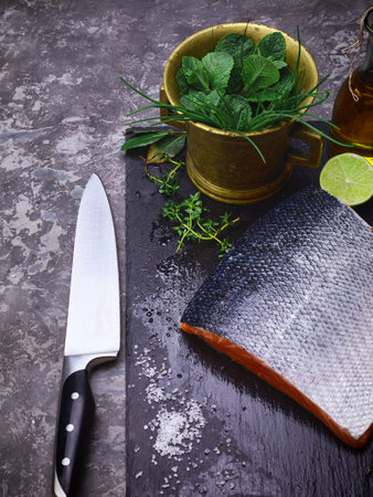 Fresh steak salmon red fish on black stone blackboard with knife cuted lime and salt olive oil fresh spicy herbs. Top view at gray concrete surface.の写真素材