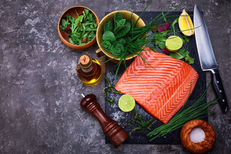 Fresh steak salmon red fish on black stone blackboard with knife cuted lime and salt olive oil fresh spicy herbs. Top view at gray concrete surfaceの写真素材
