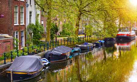 Netherlands Amsterdam. View at river Amstel with traditional houses at bank and boats at water canal. Scenic cityscape. Spring day.の写真素材