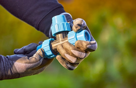 Closeup of hands in the gloves. Process of installing fittings pipes and connectors for the garden and lawn irrigation system installation. Green grass, shallow depth of field.の写真素材