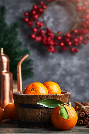 Still life with copper pitcher teapot and ripe fresh orange tangerine fruits in a wooden, barrel-shaped rustic bowl on bark wood table. Grunge stone wall berries wreath Christmas tree on background.の写真素材
