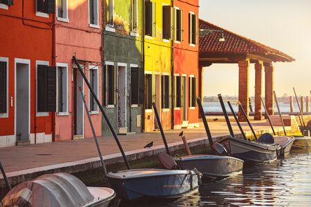 Burano island in Venice, Italy. Picturesque sunset over canal with boats among old colourful houses stone streets. Italia, popular travel destination.の写真素材