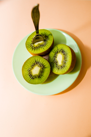 Kiwi fruits isolated on plate with dessert spoon, on pink background. Cut of green sweet kiwi. Detox, weight loss, eating vegetarian. healthy diet concept. copy spaceの写真素材