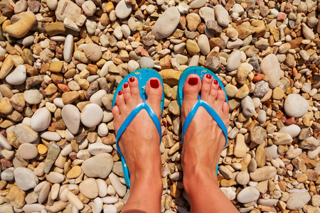 Low section of woman wearing slippers while standing on board walk.First person perspective, view on own feet. Rocky beach.Female legs wearing flip flops near sea. top viewの写真素材