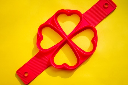 Red silicone mold on a yellow background.Silicone Heart Shape Egg Ring for Frying Pan.Frying egg with silicone form and teflon pan. molds for baking puncakes.bakery productsの写真素材
