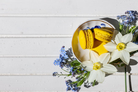 Colorful macaroons and flowers on white wooden table. Sweet macarons. Top view with copy space for...