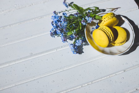 Macaroni tasty French dessert on white wooden table.macarons on vintage background. Macaron is sweet. Toned image. Copy space. tasty yellow French Macarons and forget-me-not flowersの写真素材