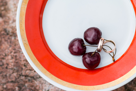 Wedding rings on plate with cherry berries. Wedding card. Valentine s Day greeting. Two golden rings and sweet fresh berries. Copy spaceの写真素材