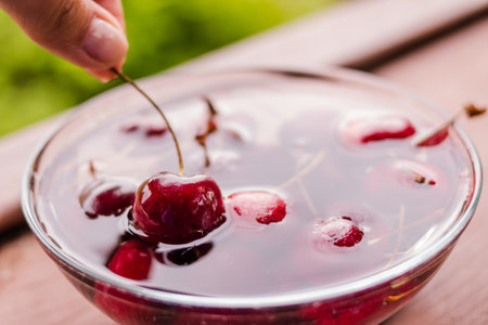 Female hands holding sweet cherries. Berry in water, in glass bowl. Raw fresh sweet cherry on wooden...