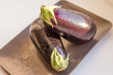 Close-up view of wet eggplants, aubergines fruit with drop water isolated on plate on white background.の写真素材