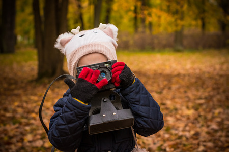 Little child with old retro camera doing photo outdoors.Portrait of little girl child with retro vintage reflex camera in park in autumn day.girl holding a cameraの写真素材