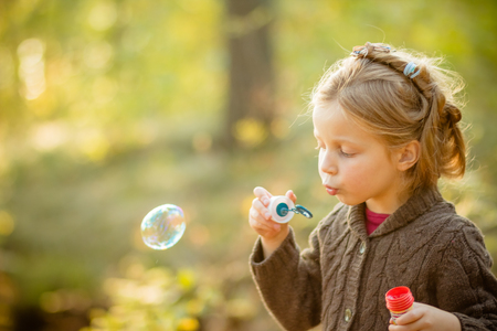 Five years old caucasian child girl blowing soap bubbles outdoor at sunset - happy carefree childhood.Fall seasom, bright colors, happy childhood. Walking in autumnal park.Copy spaceの写真素材