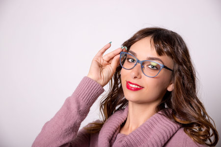 Beautiful brunette girl with red lips and wearing glasses with a blue frame smiling on a white...