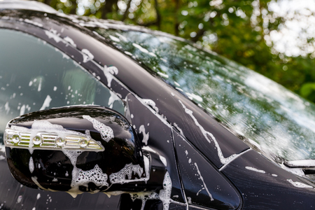 Car wash with soap.Car washing process of luxury black car full covered with white foam and bubbles.modern car covered with foam in car wash.Selective focus.Copy spaceの写真素材