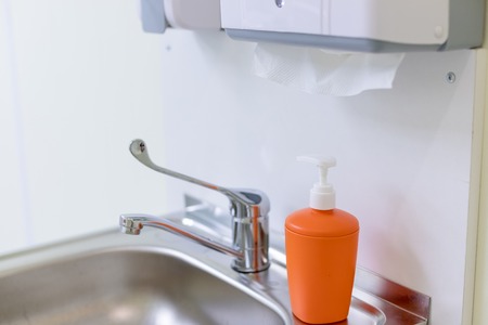 Orange bottle for liquid soap in dentist, doctor office. metal sink, liquid soap, paper towels.Health and Hygiene concept. copy space.container with liquid soap. The place for washing of hands. Concept hygiene and purity of hands.の写真素材