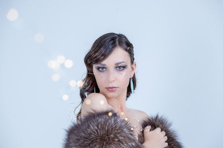Dreaming winter woman looking up and wearing fur hat.Fashion portrait of beautiful sexy woman model with creative make-up in luxury fur coat.bare shoulders.Winter fashion sale.Luxurious brunette in standing in coatの写真素材