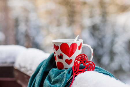 Hot chocolate or coffee, red heart near the cup, winter background with lights out of focus. Winter or Valentines day background.greeting card. White mug of hot drink and red felt heart.Copy spaceの写真素材