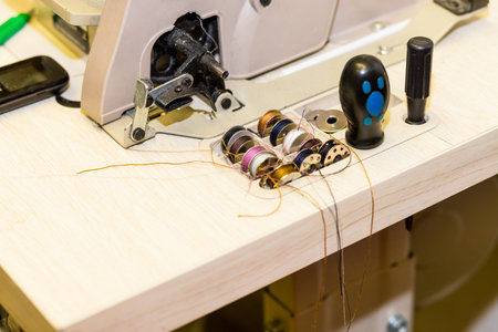 box with metal spools of colored threads near sewing machine. And one loaded into machine. Tailor...