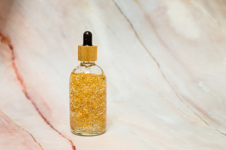 Face cream with pearl particles.Golden mask,Moisturizing anti-ageing face-care serum with gold particles in luxury glass container with golden lid, isolated on marble background.Glass golden transparent jar with primer oilの写真素材