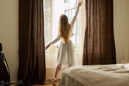 Hand Opens Curtain on the Wooden Cottage House Window. Bright Sunlight Shines Through. Beautiful snowy Winter morning light behind the Chalet Window.の写真素材