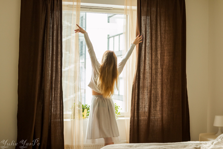 Hand Opens Curtain on the Wooden Cottage House Window. Bright Sunlight Shines Through. Beautiful snowy Winter morning light behind the Chalet Window.の写真素材