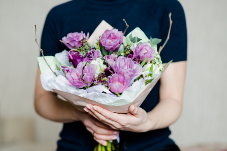 florist woman holding a beautiful colourful blossoming flower bouquet of fresh white pink tulips, ranunculus,leaves on the grey wall background.bouquet of spring flowers in her hands. Mothers day conceptの写真素材