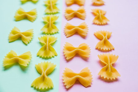 Bow tie Italian pasta fartalle pattern isolated on colorful background, top view. Dry uncooked...