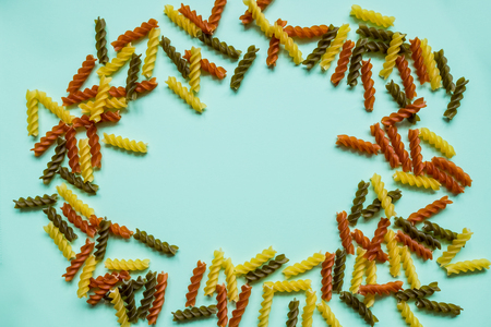 Frame from wheat pasta on red background. Random pattern. Flat lay.Variety of types and shapes of dry Italian pasta.extured Italian food background - colorful uncooked penne pasta on wooden table. Top viewの写真素材
