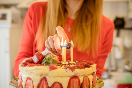 Mothers hand lighting candles in birthday cake.Mothers Day.Cake with strawberry.Hand of woman lights...
