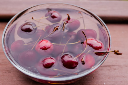 Red sweet fresh cherries splashed in water on wooden background with a reflection in the water....